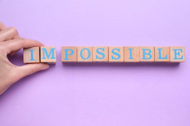Motivasyon konsepti. Kadın, menekşe arkaplanındaki tahta küpleri kaldırarak sözcüğü imkansızdan olanaksıza çeviriyor, üst görünüm