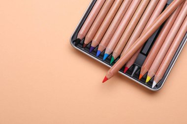 Renkli pastel kalemler bej arka planda kutuda, üst görünümde yazı için yer var. Malzemeler çiziliyor