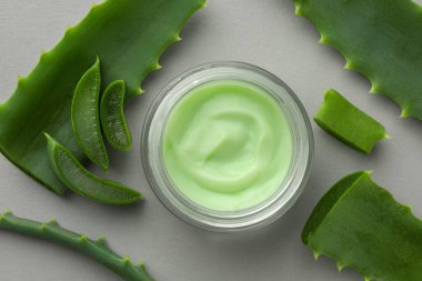 Açık gri arkaplanda kremalı ve kesilmiş aloe yapraklı kavanoz, düz uzanmış