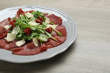 Bir tabak lezzetli Bresaola salatası, kurutulmuş domatesler ve ahşap masada parmesan peyniri, yakın plan. Metin için boşluk