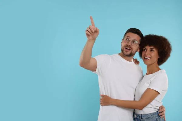 International dating. Lovely couple pointing at something on light blue background, space for text