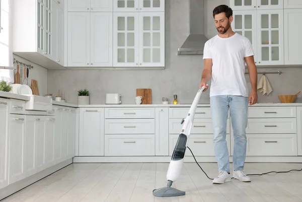 Happy man cleaning floor with steam mop in kitchen at home. Space for text