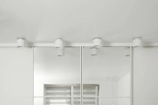 Stylish lamps near mirror on white ceiling