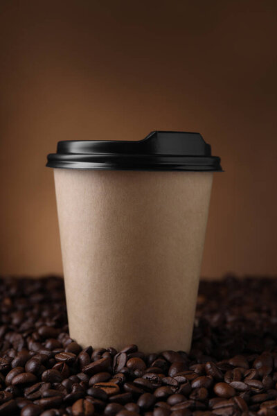 Coffee to go. Paper cup on roasted beans against brown background