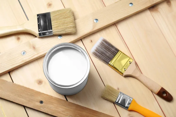Can of white paint and brushes on wooden table, above view