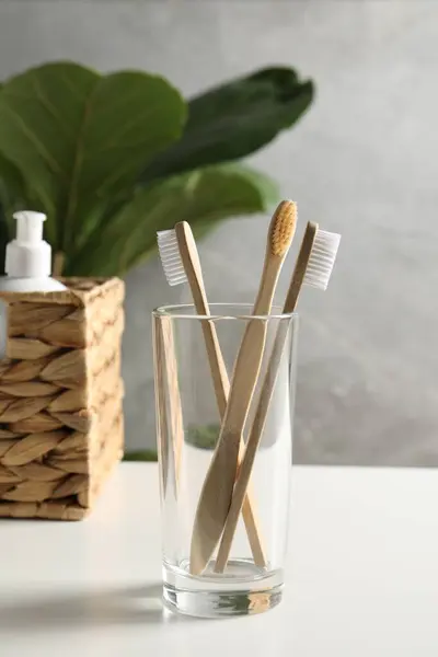 Bamboo toothbrushes in glass holder on white countertop