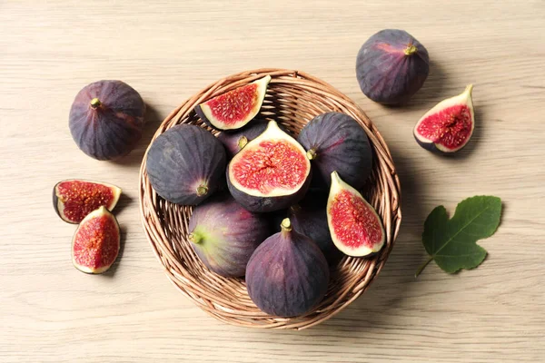 Whole and cut ripe figs with leaf on wooden table, flat lay