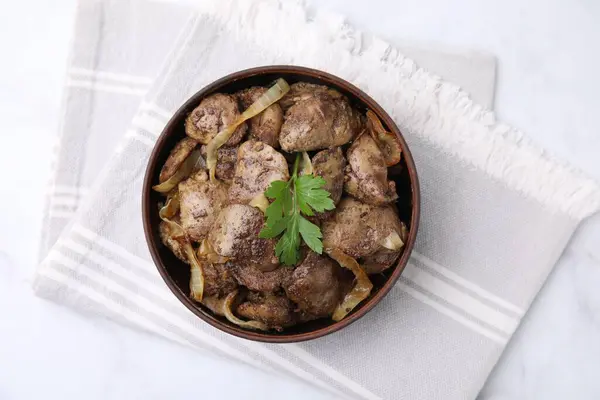 Tasty fried chicken liver with onion and parsley in bowl on white table, top view