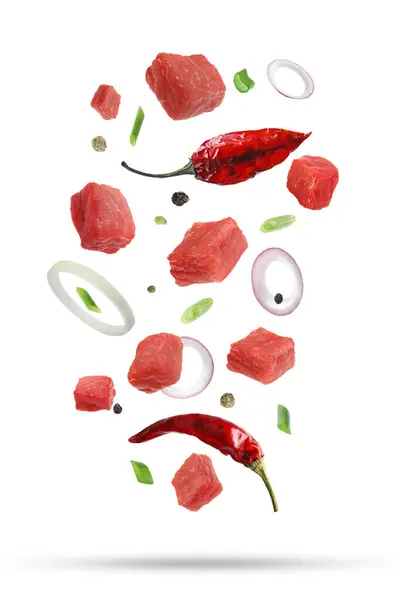 Pieces of raw beef and other ingredients for goulash falling on white background