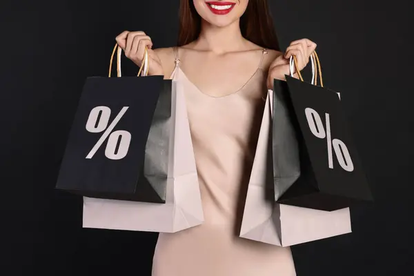 Discount, sale, offer. Woman holding paper bags with percent signs against black background, closeup