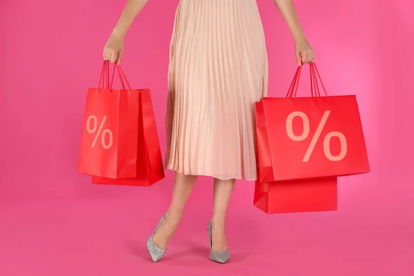 Discount, sale, offer. Woman holding paper bags with percent signs against pink background, closeup