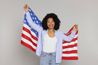 4 Temmuz - ABD 'nin Bağımsızlık Günü. Açık gri arka planda Amerikan bayrağı taşıyan mutlu kadın.