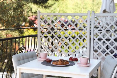 Terastaki beyaz masada çay ve kruvasanla açık hava kahvaltısı.