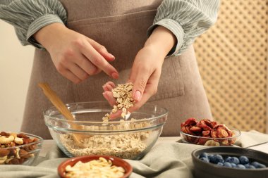 Tahıl yapıyorum. Kadın mutfaktaki masada kaseye yulaf gevreği koyuyor, yakın plan.