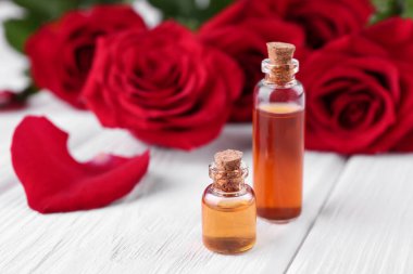 Beyaz ahşap masa üzerinde gerekli yağ şişeleri ve kırmızı gül çiçekleri, yakın plan. Metin için boşluk