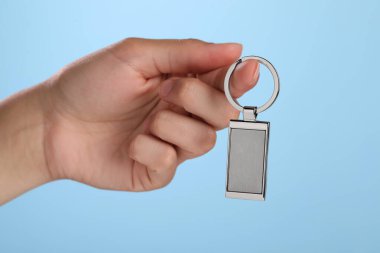 Açık mavi arkaplanda metalik anahtarlık tutan kadın, yakın plan.