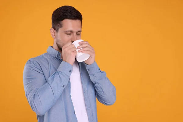 Man drinking from white mug on orange background. Space for text
