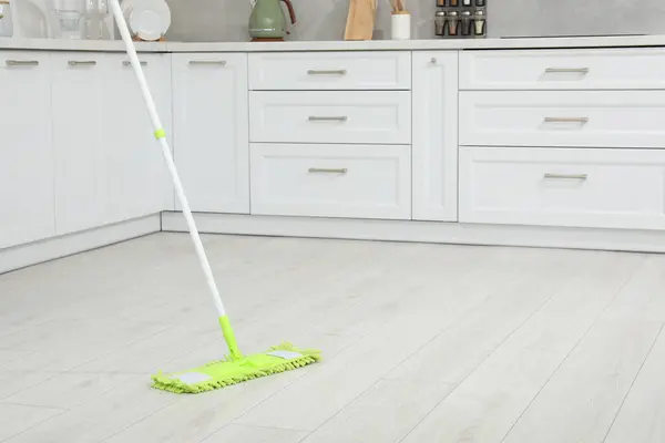 Cleaning of parquet floor with mop in kitchen, space for text