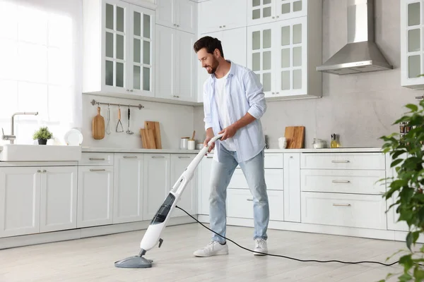 Happy man cleaning floor with steam mop in kitchen at home