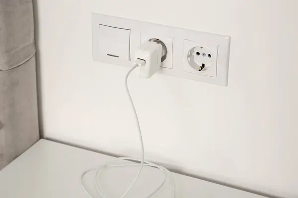 Plug in power socket and light switch on white wall indoors