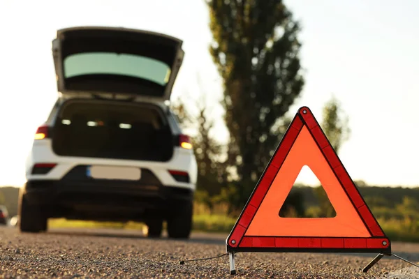 Warning triangle and broken car on roadside, selective focus