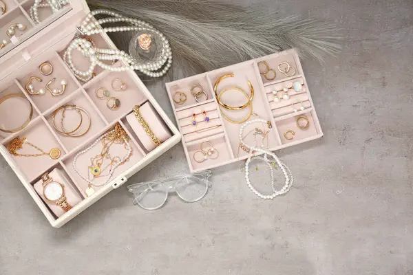 Jewelry boxes with many different accessories, glasses and perfume on light grey table, flat lay. Space for text