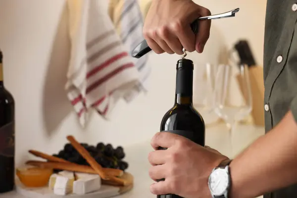 Romantic dinner. Man opening wine bottle with corkscrew in kitchen, closeup