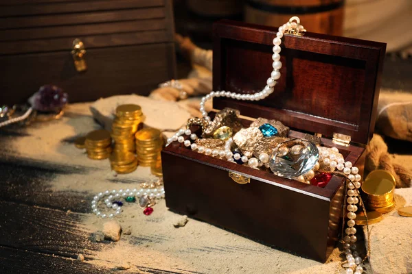 Chest with treasures and scattered sand on wooden table