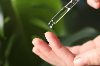 Kadın arka plandaki bulanık parmağa kozmetik serumu uyguluyor. Yakın plan. Metin için boşluk