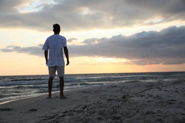 Deniz kenarındaki kumlu sahilde gün batımında, arka manzara