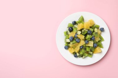 Pembe arka planda lezzetli meyve salatası tabağı, üst manzara. Metin için boşluk