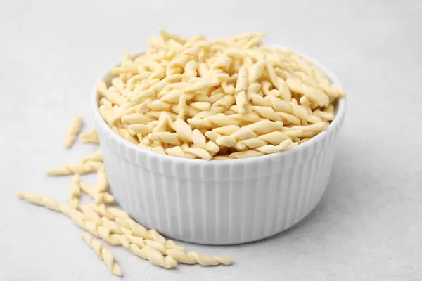 stock image Bowl with uncooked trofie pasta on light grey table, closeup