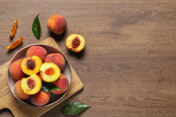 Delicious juicy peaches and leaves on wooden table, flat lay. Space for text