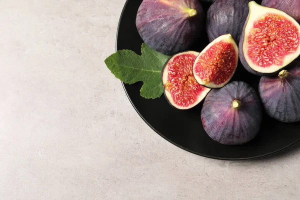 Whole and cut ripe figs with leaf on light grey textured table, top view. Space for text