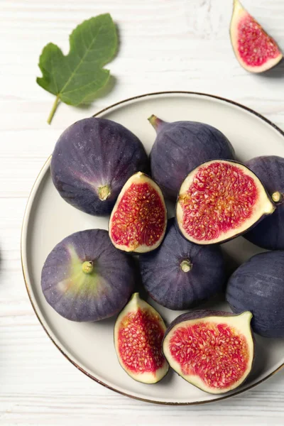 Whole and cut ripe figs with leaf on white wooden table, flat lay