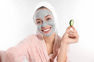 Yüz maskeli ve salatalık dilimli bir kadın beyaz arka planda selfie çekiyor. Spa tedavileri