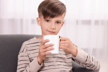 Evdeki kanepede beyaz seramik bardaklı tatlı çocuk.