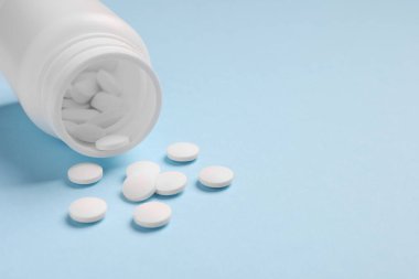 Açık mavi arka planda hapları olan plastik tıbbi şişe, yakın plan. Metin için boşluk