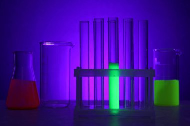 Mor arka planda parlak sıvılar bulunan laboratuvar camları.