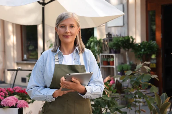 stock image Smiling business owner with tablet near her flower shop outdoors, space for text