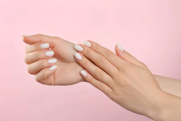 Woman with white polish on nails against pink background, closeup
