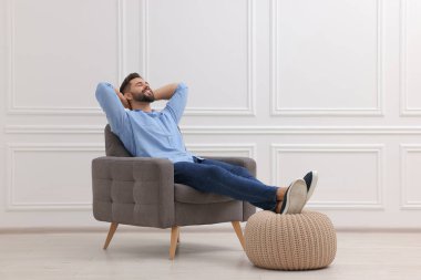 Beyaz duvarın yanındaki koltukta dinlenen yakışıklı adam.