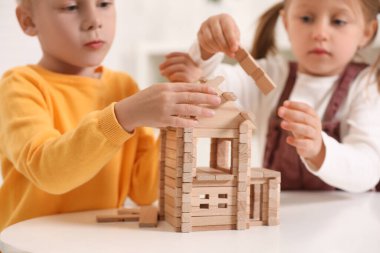 Küçük çocuk ve kız, beyaz masada ahşap evle oynuyorlar, seçici bir odak. çocuk oyuncakları