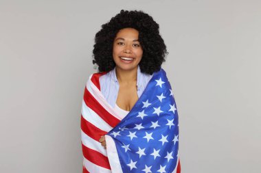 4 Temmuz - ABD 'nin Bağımsızlık Günü. Açık gri arka planda Amerikan bayrağı taşıyan mutlu kadın.