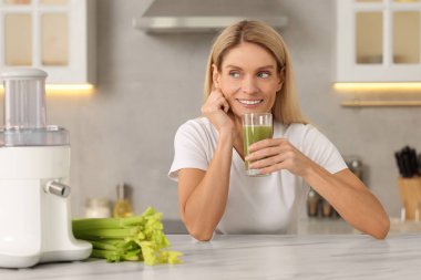 Mutfaktaki masada elinde bir bardak taze kereviz suyu olan bir kadın.