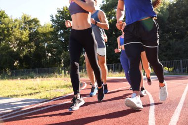 Güneşli bir günde stadyumda koşan bir grup insan, yakın çekim.