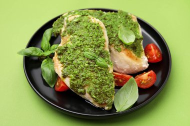 Pesto soslu leziz tavuk göğsü, açık yeşil masada domates ve fesleğen, yakın plan.