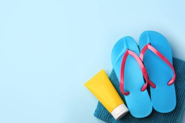 Açık mavi arkaplanda havlu, güneş kremi ve parmak arası terlikler, metin için boş alan. Plaj aksesuarları