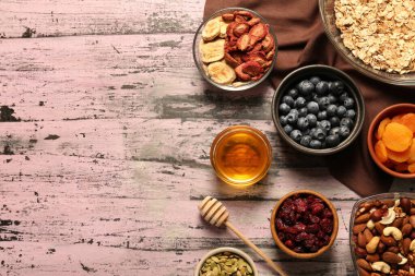 Tahıl yapıyorum. Yulaf gevrekleri, kurutulmuş meyveler ve pembe ahşap masa üzerindeki diğer malzemeler, düzlük ve metin için yer.