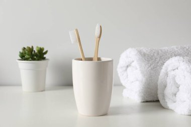 Bambu diş fırçaları kabın içinde, saksı bitkisi ve havlular beyaz tezgahın üzerinde.